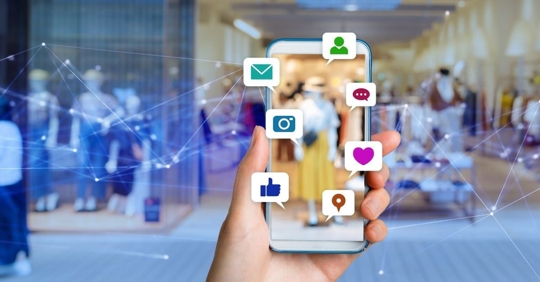 artwork of a person holding a cellular device with icons floating around, including email, messages, camera, thumbs up, and heart